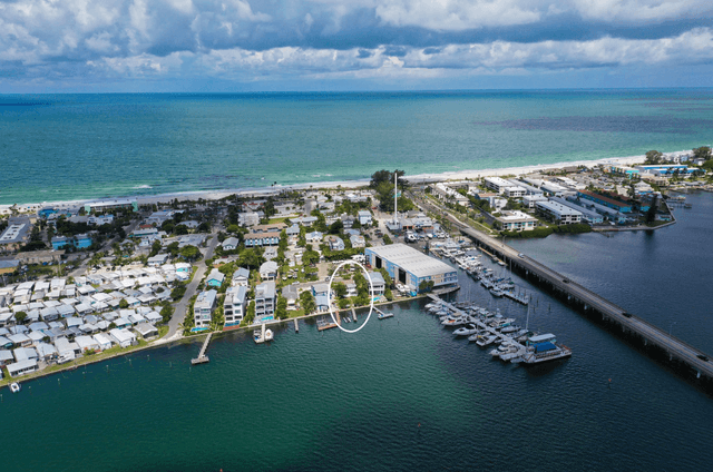 Stunning aerial view showcases waterfront properties nestled between pristine beaches and protected marina, offering the perfect coastal getaway location.