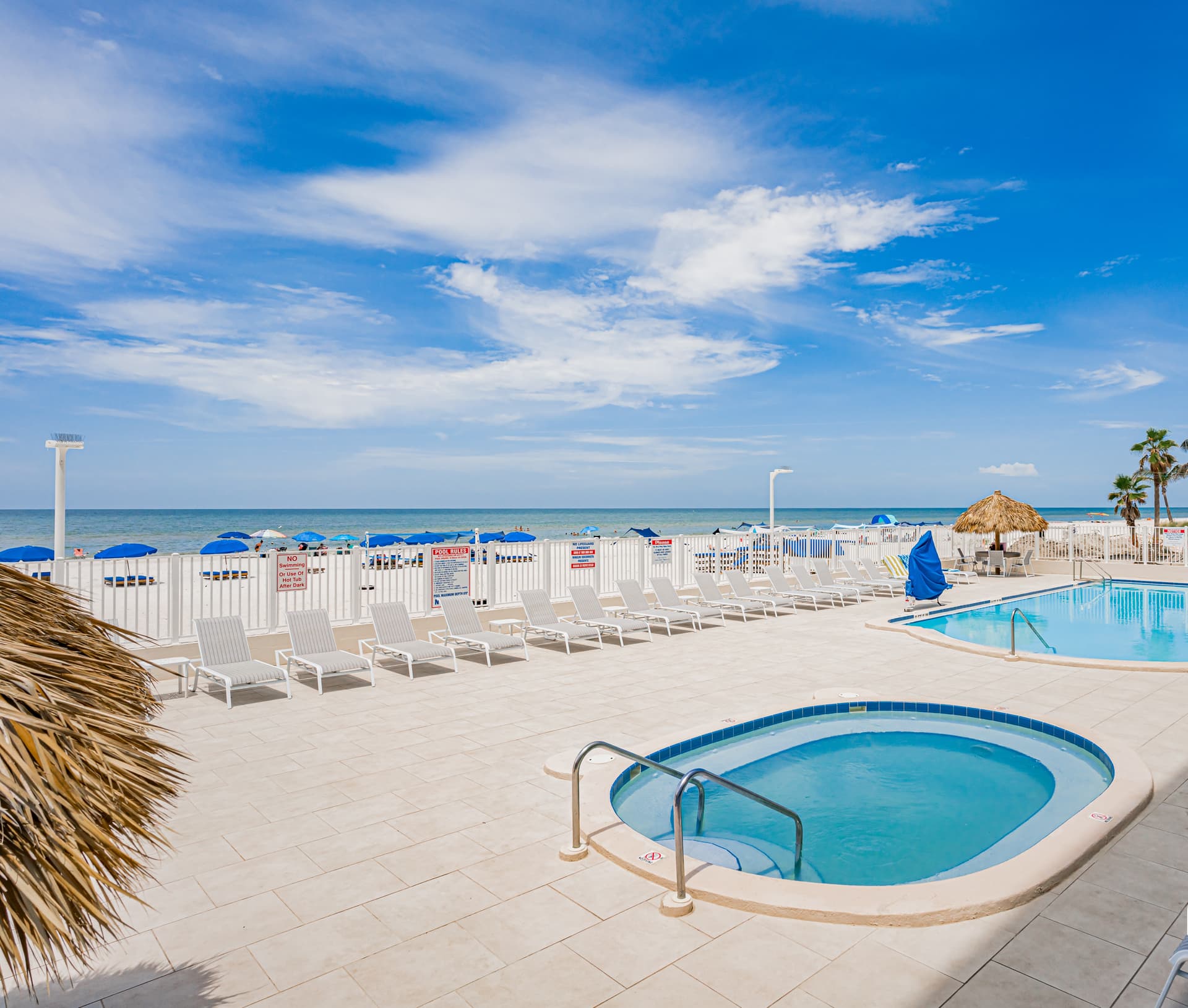 Beachfront pool deck with hot tub overlooking pristine white sand and turquoise waters.