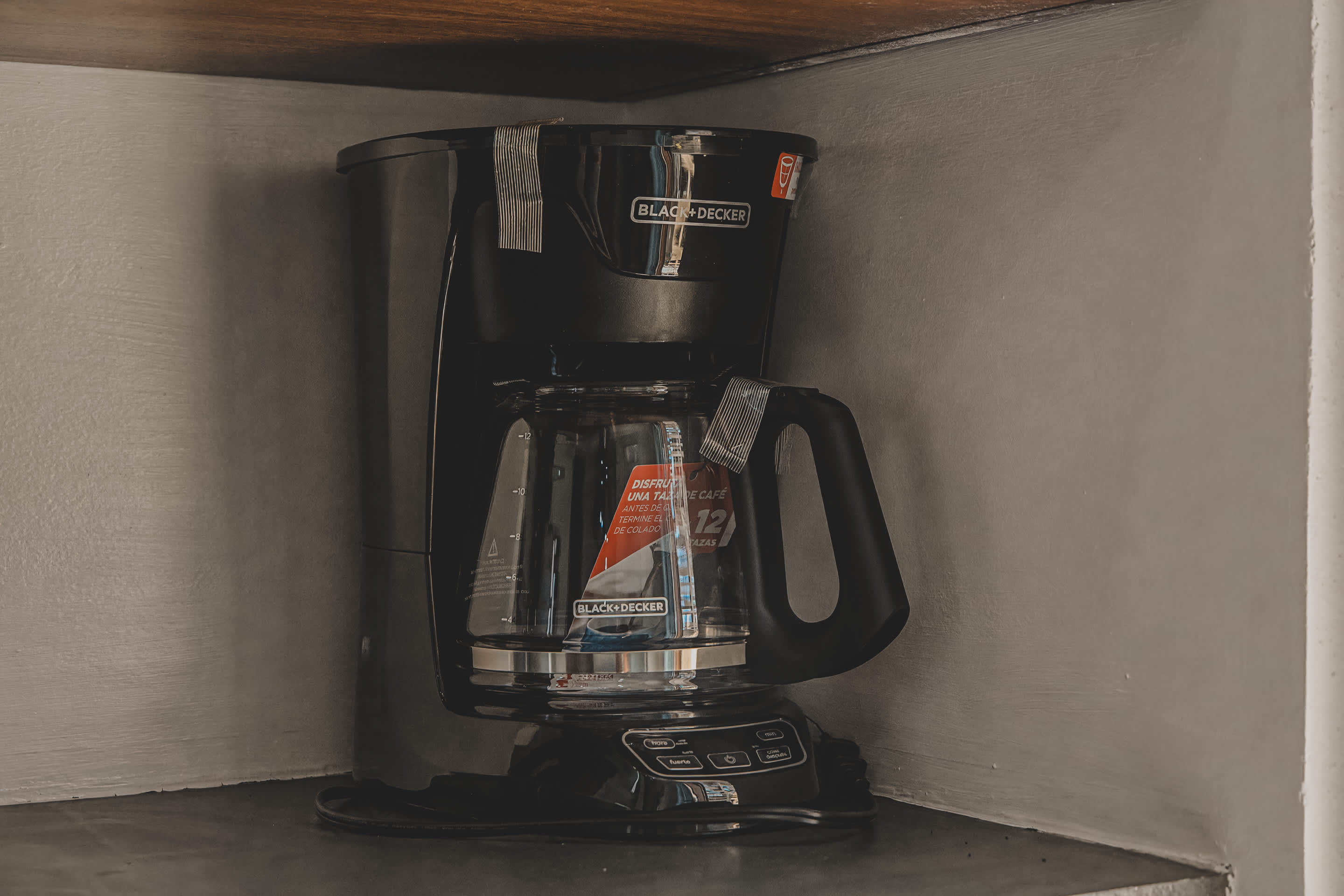 Black and silver Black+Decker drip coffee maker with a glass carafe, sitting on a dark countertop in a corner.