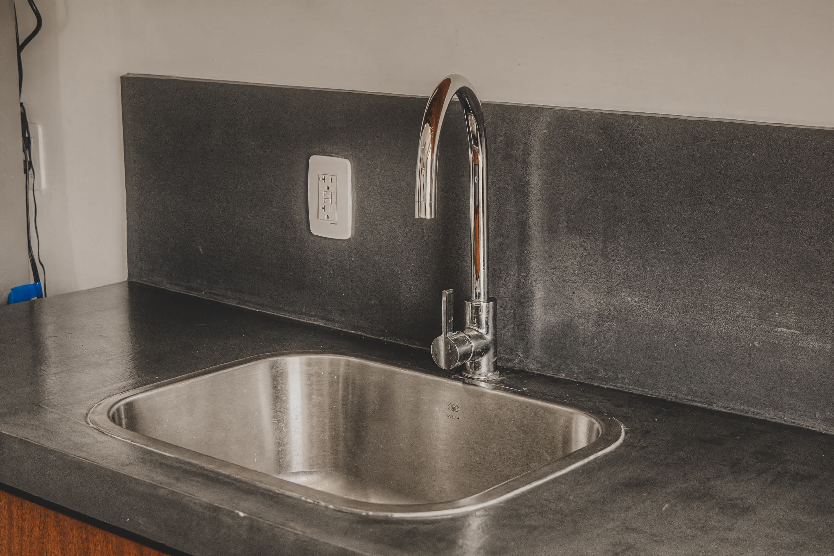 Stainless steel kitchen sink with a modern chrome faucet, set into a dark concrete countertop with a matching backsplash.