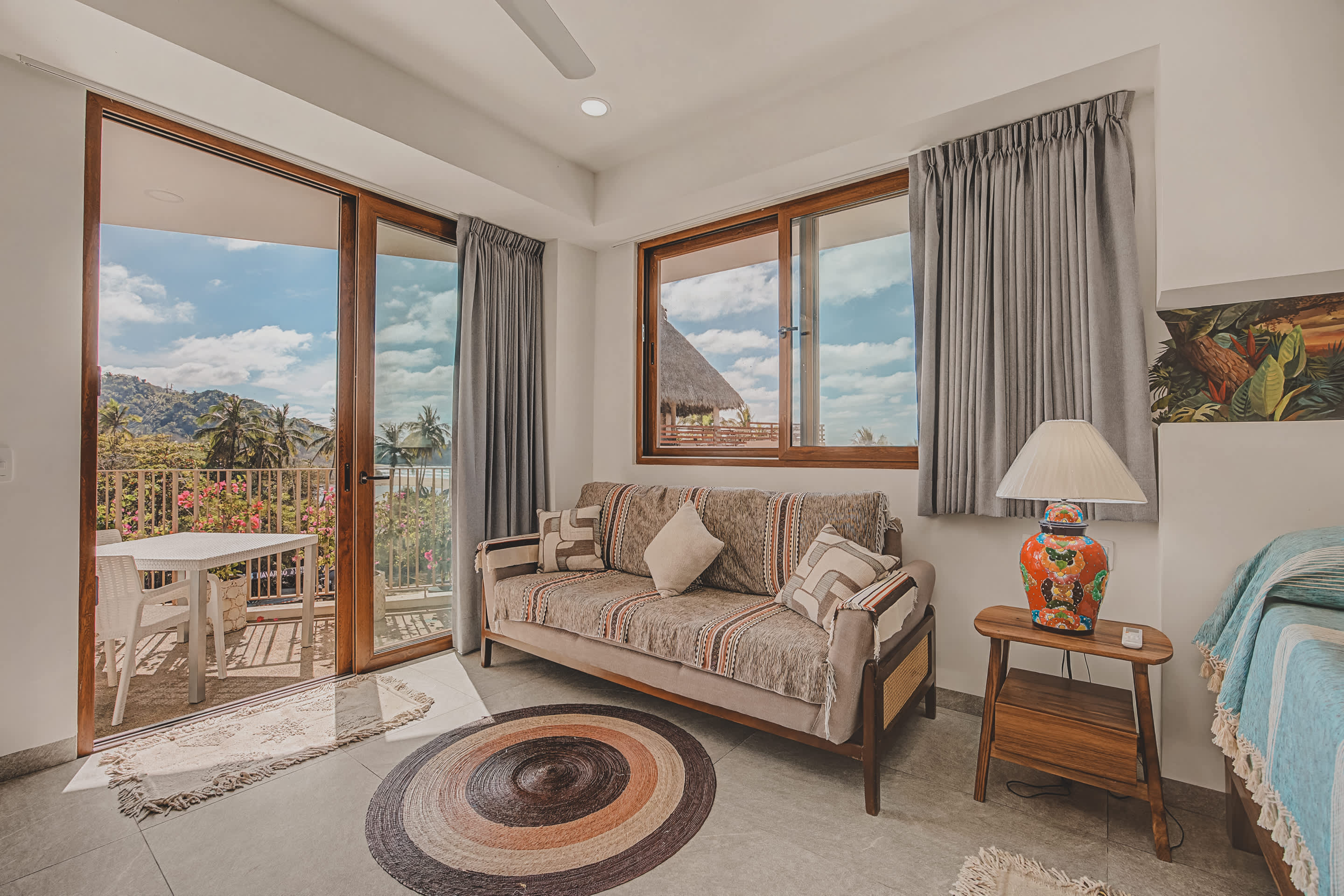 This bedroom offers a comfortable sofa and a bed, with a large sliding glass door opening directly onto the balcony, allowing natural light and views of the outdoor scenery.