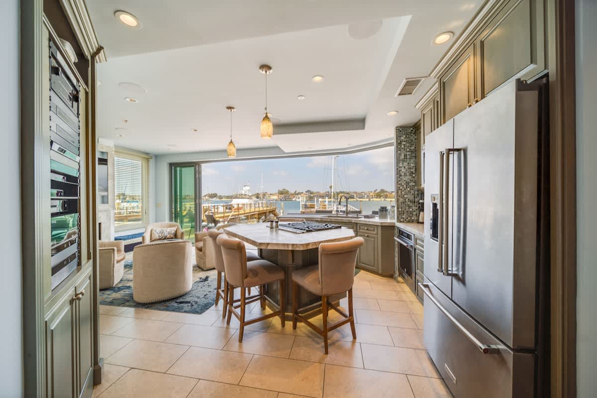 View from the kitchen showcasing the open-concept layout, with the octagonal island in the foreground, leading to the living area with armchairs and large sliding glass doors opening to the bayfront.