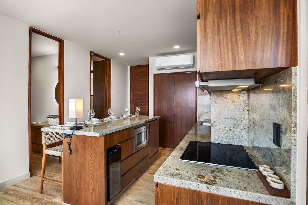 A functional kitchen island with a light granite countertop provides bar seating and houses a microwave and beverage cooler, complementing the built-in stovetop and oven. The space features rich wooden cabinetry and an open layout connecting to the living area.