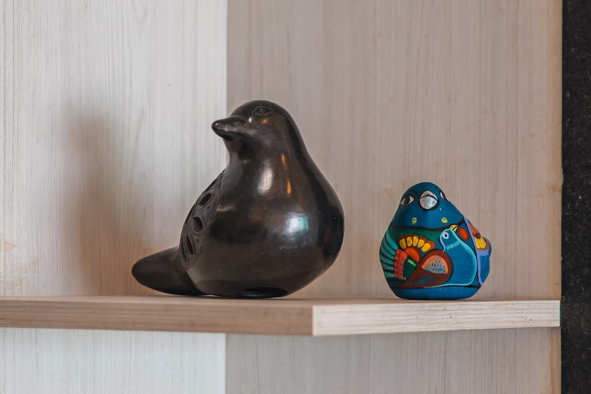 Two charming decorative bird figurines displayed on a light wooden shelf; one is a larger, glossy black ceramic bird, and the other is a smaller, colorful hand-painted bird, adding artistic flair to the interior.