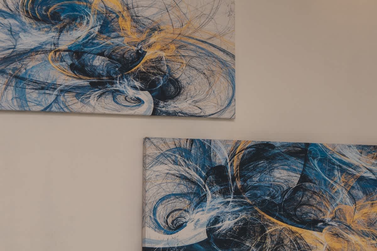 Two abstract art canvases displayed on a light wall, showcasing dynamic swirling patterns in shades of blue, yellow, and black, creating a modern and vibrant aesthetic.