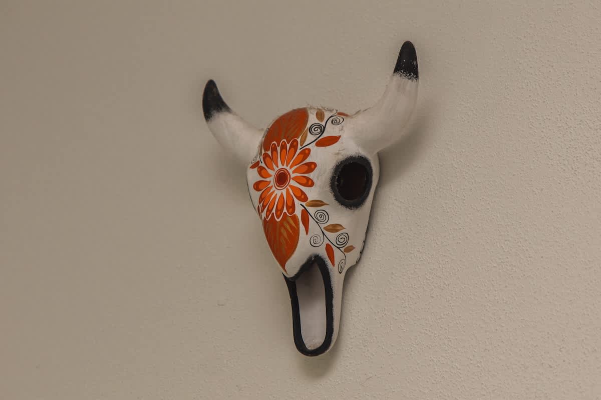 A unique decorative wall sculpture resembling a bull skull, painted white with intricate orange floral patterns and dark accents on the horns and eye sockets, adding a cultural touch.