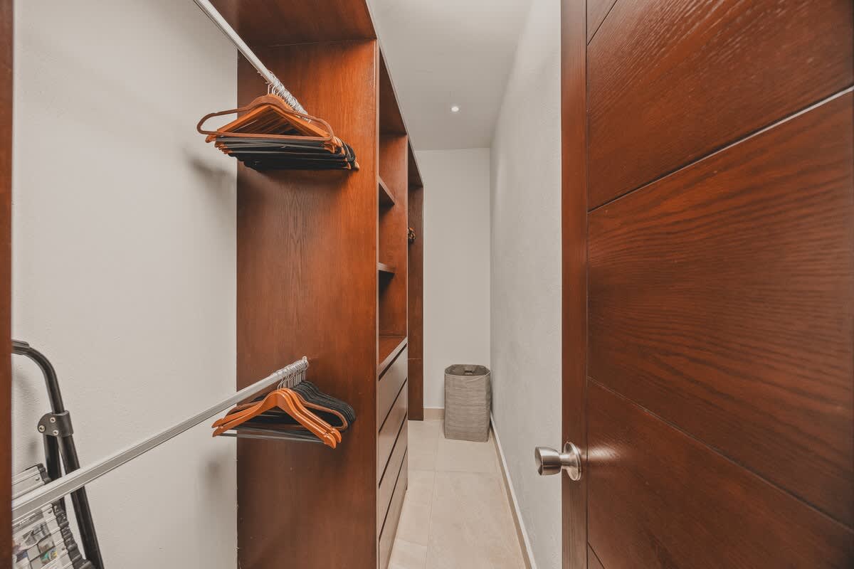 A functional walk-in closet with built-in wooden shelving and hanging rods, providing ample storage space for clothes and luggage. A laundry hamper is visible in the corner.