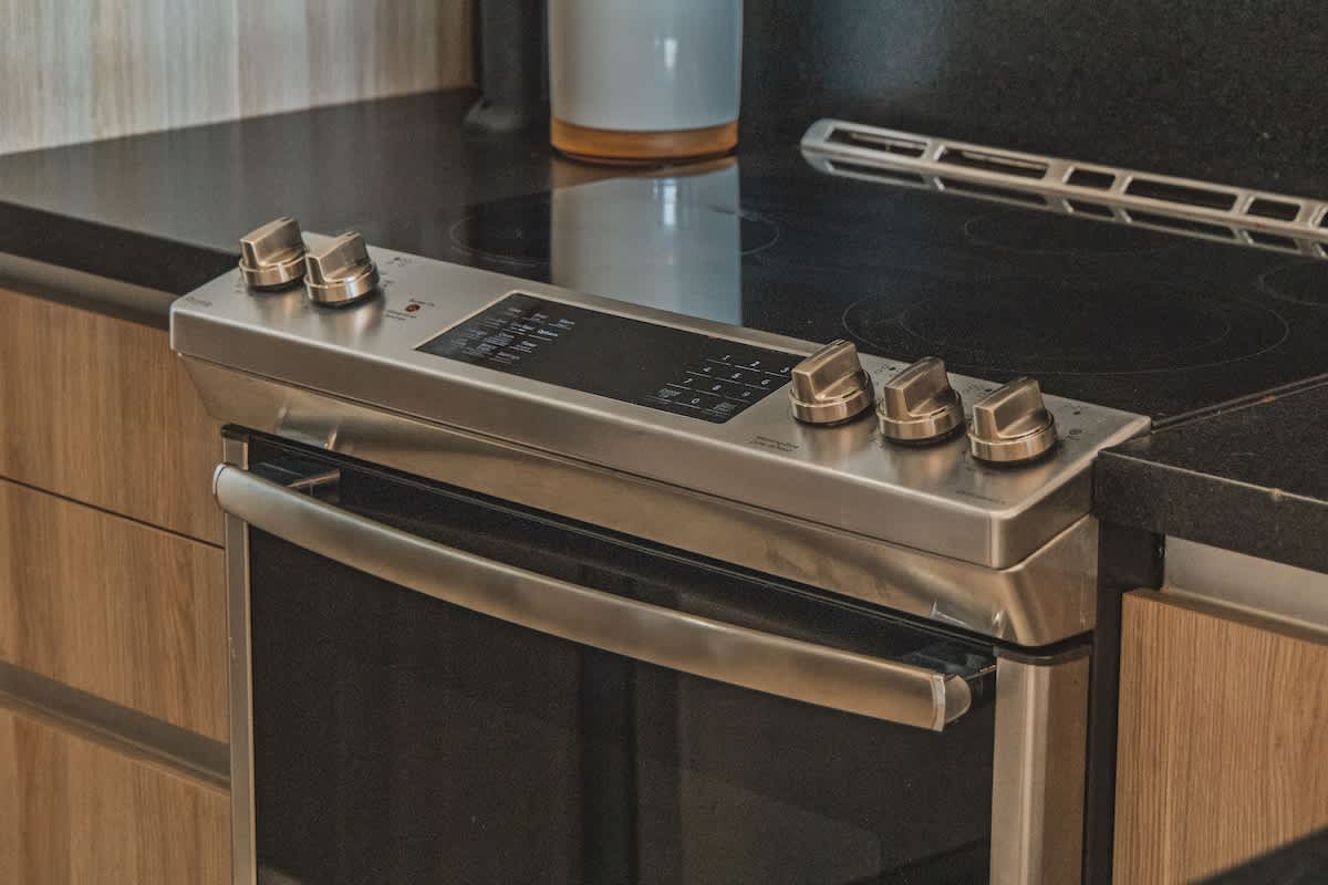 A modern stainless steel electric range with a sleek black glass cooktop and control panel, seamlessly integrated into a kitchen counter with dark granite countertops and light wood cabinetry, offering contemporary cooking facilities.