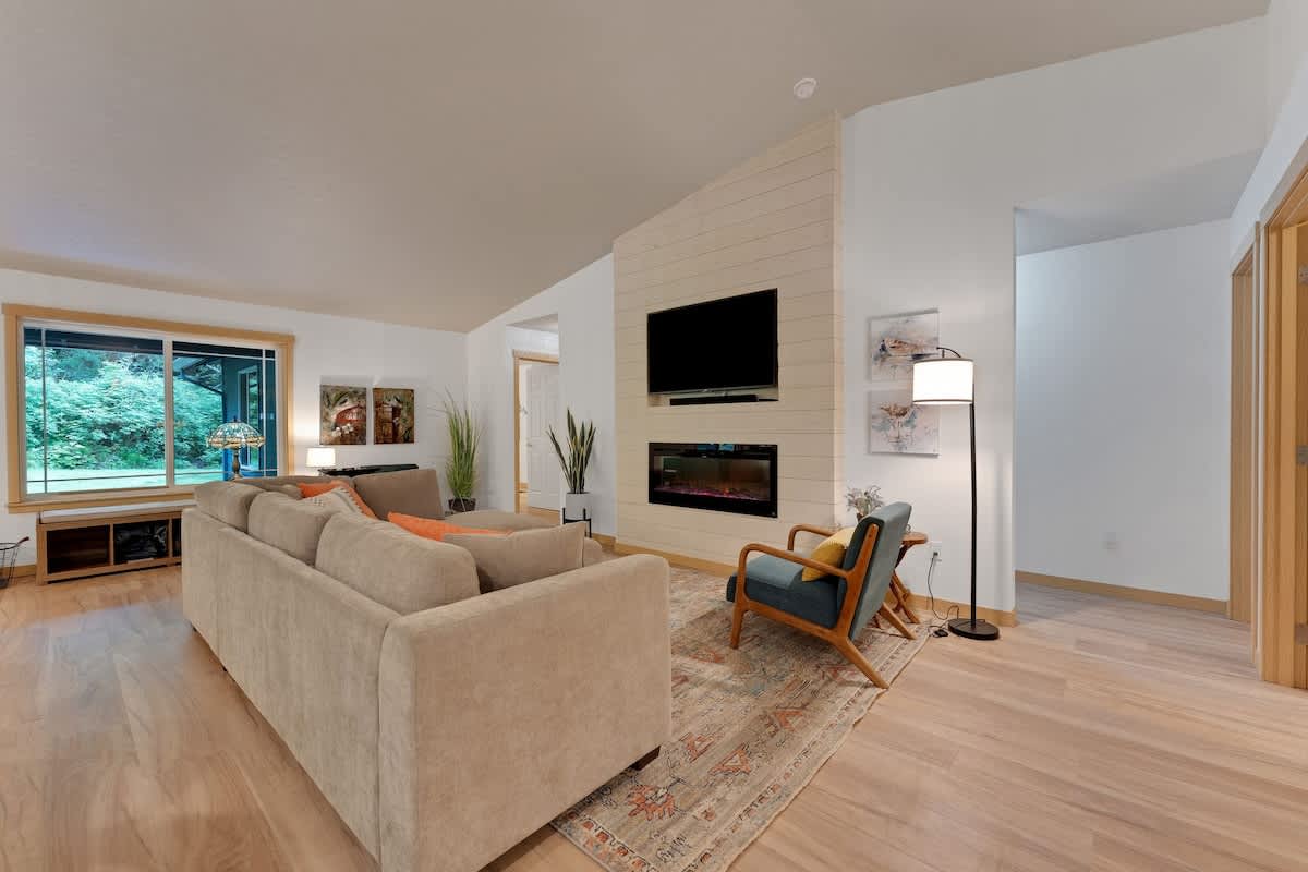 A cozy living room featuring a large, light-colored sectional sofa, an accent chair, and a modern fireplace with a mounted television above, set against a shiplap-style accent wall.