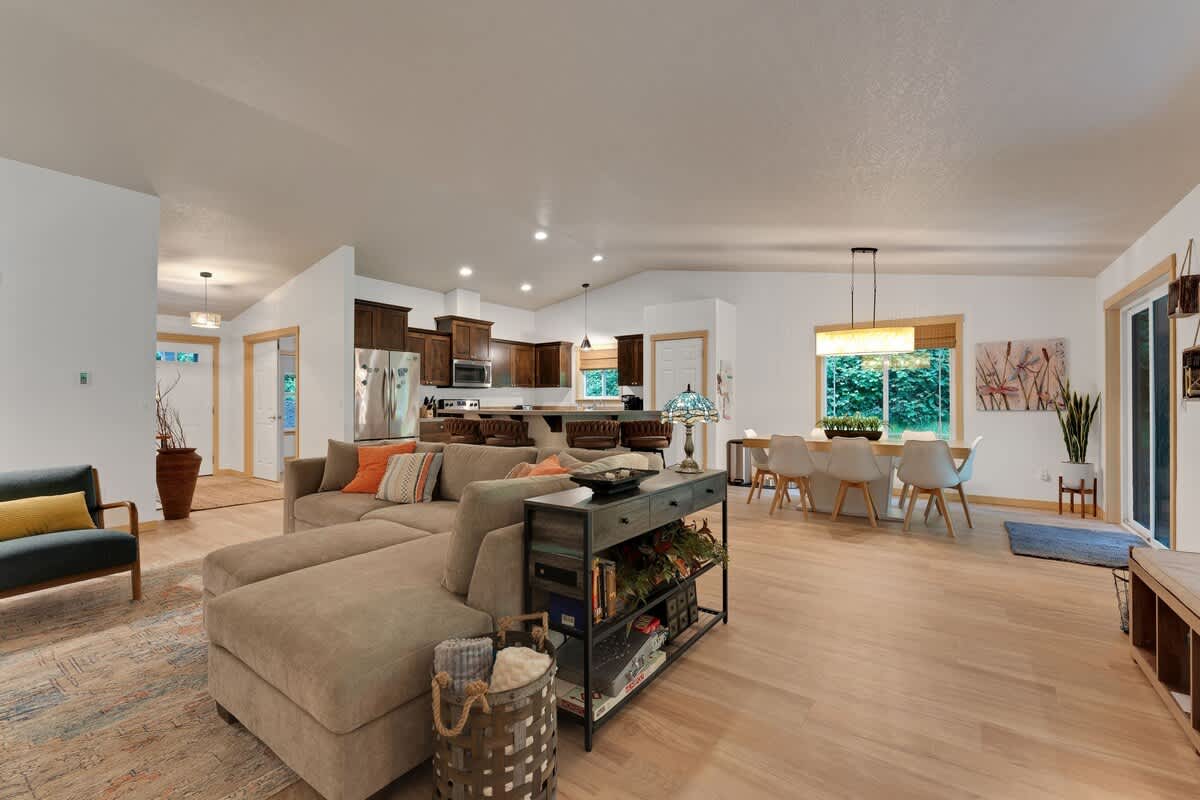 A panoramic view of the open-concept living space, showcasing the kitchen with a breakfast bar, a spacious living room with a sectional sofa, and a dining area, all connected by light hardwood floors.