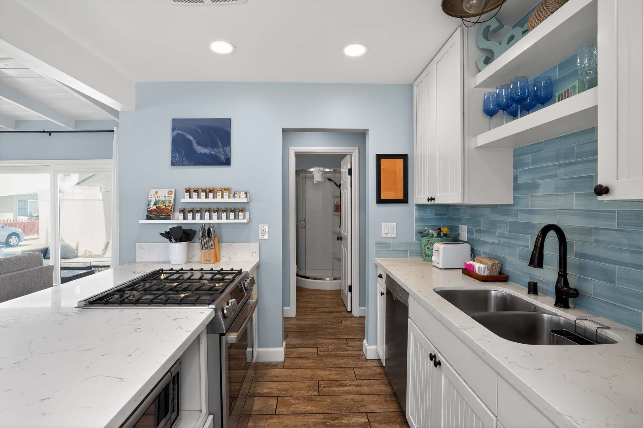 The kitchen features white cabinets, light blue subway tile backsplash, and a gas cooktop on a white quartz island, with a doorway leading to what appears to be a bathroom or utility room.