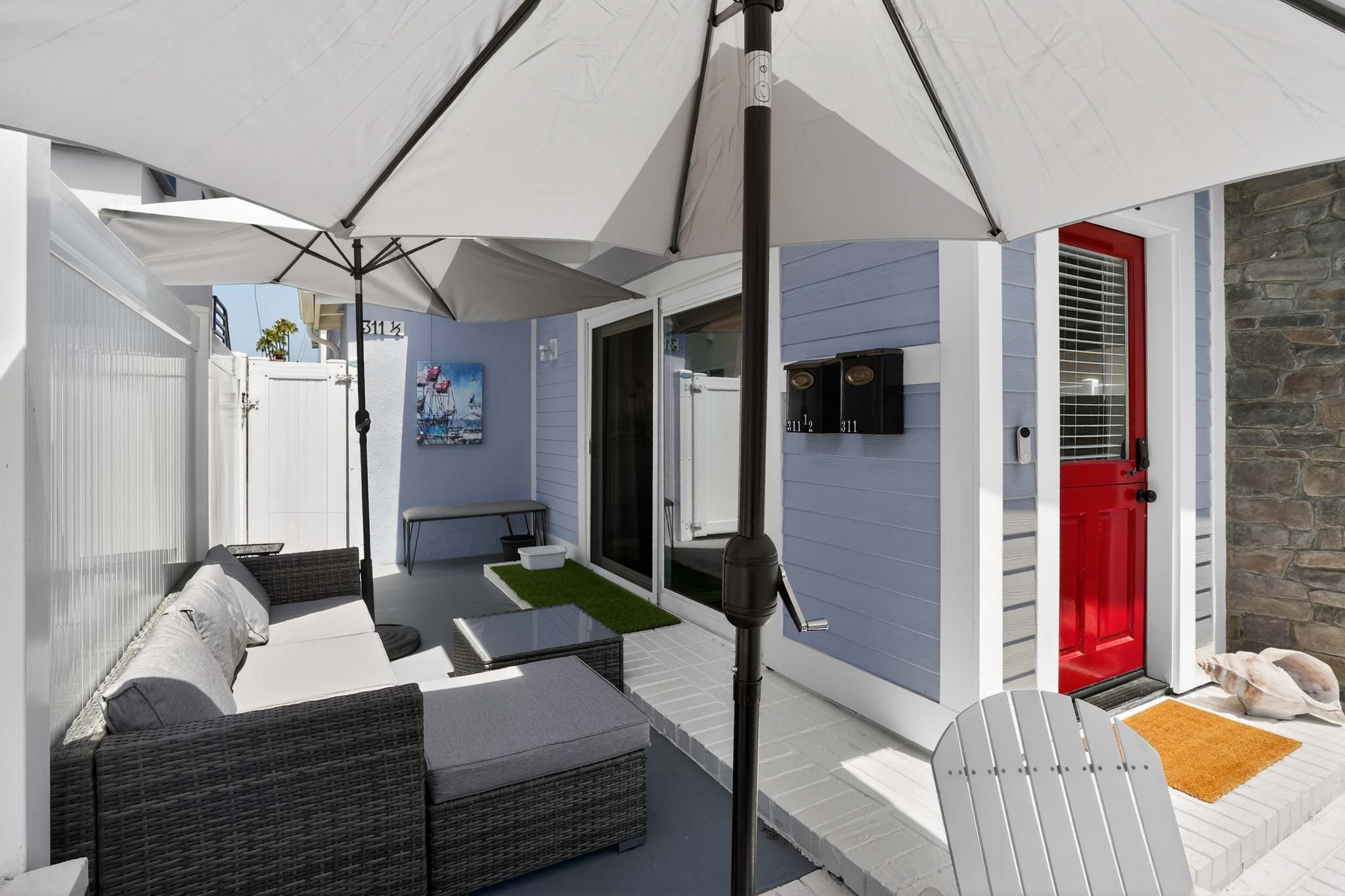 Front patio area showcasing wicker outdoor furniture and large patio umbrellas, with a sliding glass door providing access to the interior and a red front door visible nearby.