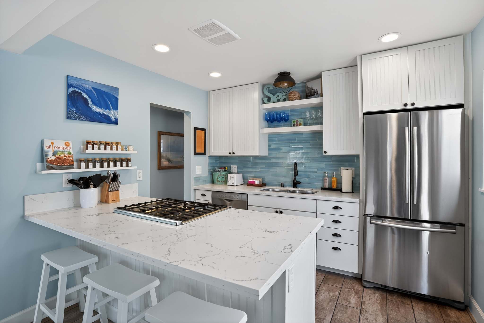 A modern kitchen features white shaker cabinets, light blue subway tile backsplash, white quartz countertops, and stainless steel appliances including a gas range on the island and a French door refrigerator.