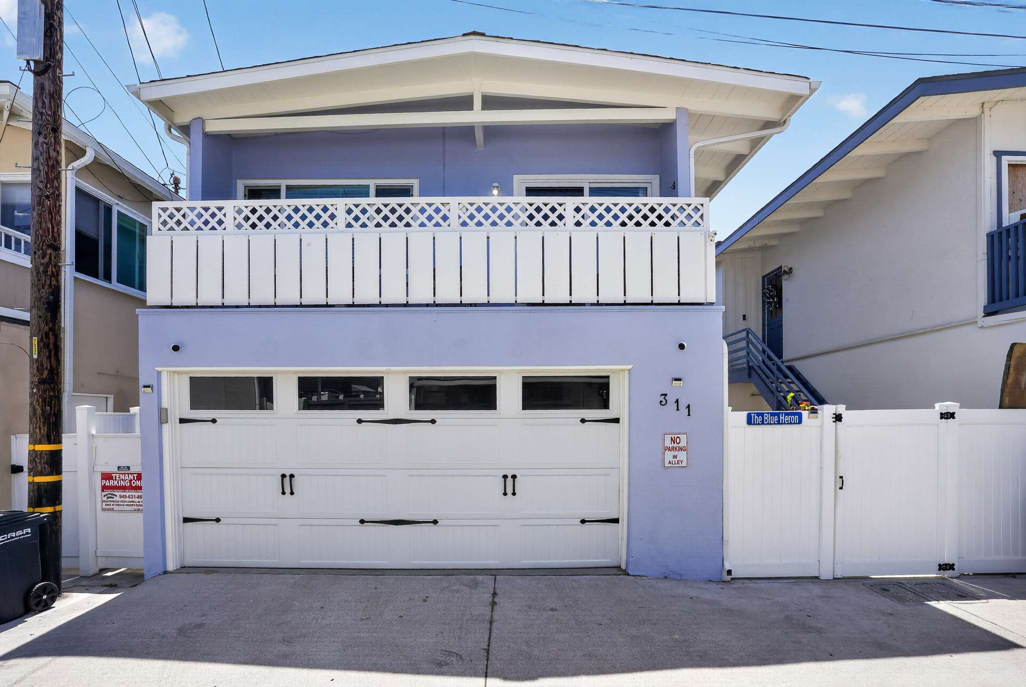 Rear exterior of a light blue house featuring a white garage door with windows and a balcony above with a white lattice railing. The house number "311" is visible next to the garage.
