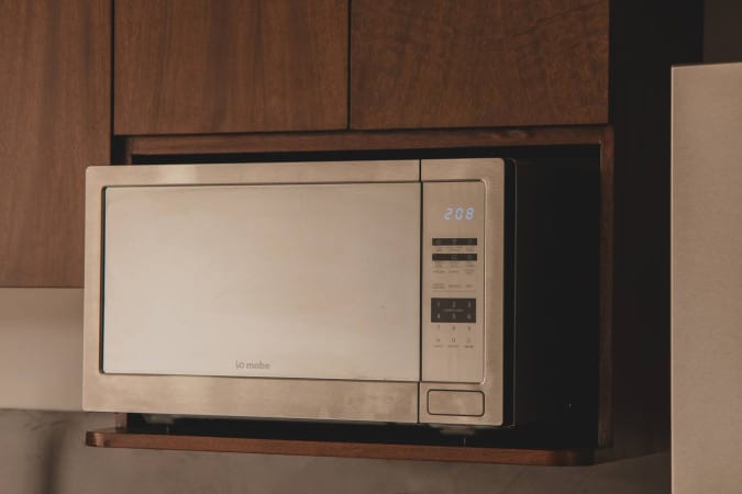 Stainless steel microwave with a digital display showing "2:08", built into a dark wooden cabinet above a counter.