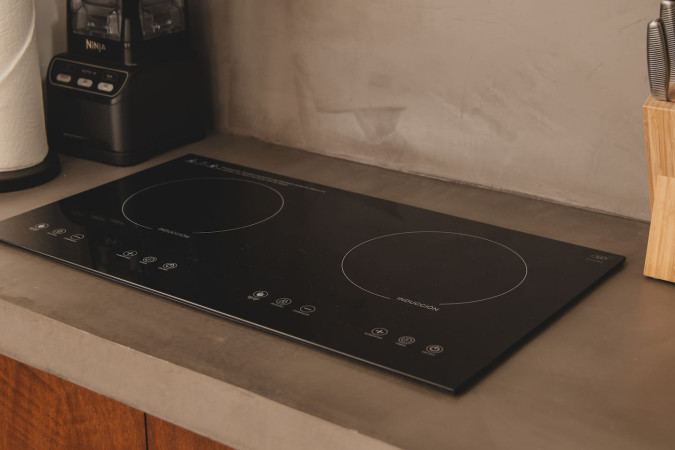 Sleek black induction cooktop with two burners and touch controls, integrated into a light gray concrete countertop.