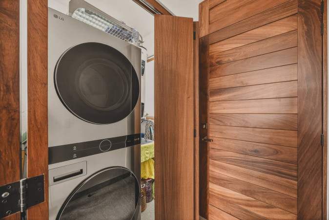 Compact laundry area featuring a stacked silver washer and dryer unit, neatly tucked behind a wooden door, with a glimpse of storage space beyond.