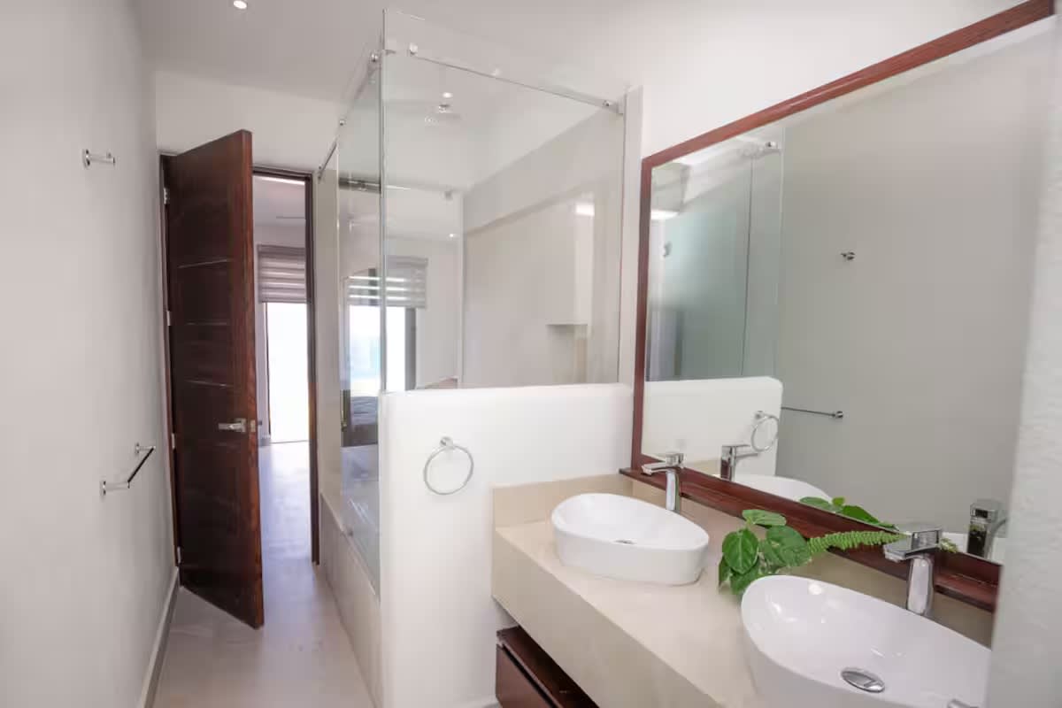 Modern bathroom featuring a double vanity with two white vessel sinks set on a light countertop, a large wooden-framed mirror, and a clear glass shower enclosure.