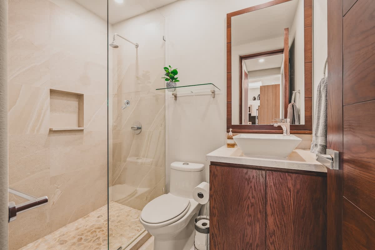 A modern bathroom featuring a glass-enclosed shower with pebble flooring and a built-in niche. A dark wood vanity with a white vessel sink and a large mirror completes the space.