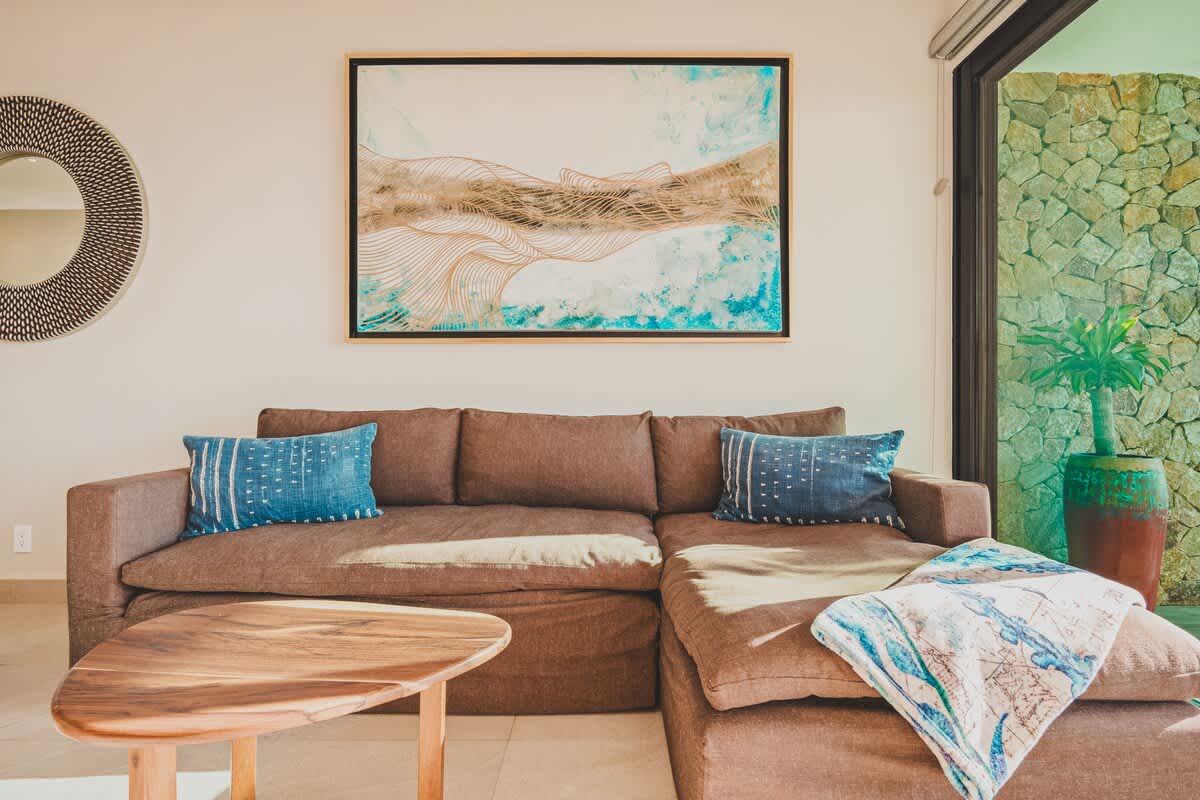 Cozy living area featuring a large brown sectional sofa adorned with blue throw pillows and a patterned blanket, a unique wooden coffee table, and a large abstract artwork on the wall.