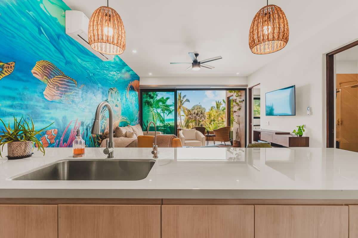 Kitchen island with a stainless steel sink and faucet, offering a view into the living area with a vibrant underwater mural and sliding glass doors opening to an ocean view.