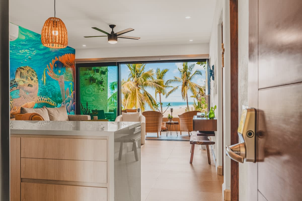 The open-concept living area and kitchen are visible from the entryway, featuring a large kitchen island, a vibrant underwater mural, and sliding glass doors leading to a balcony with ocean views. Modern pendant lights hang above the island.