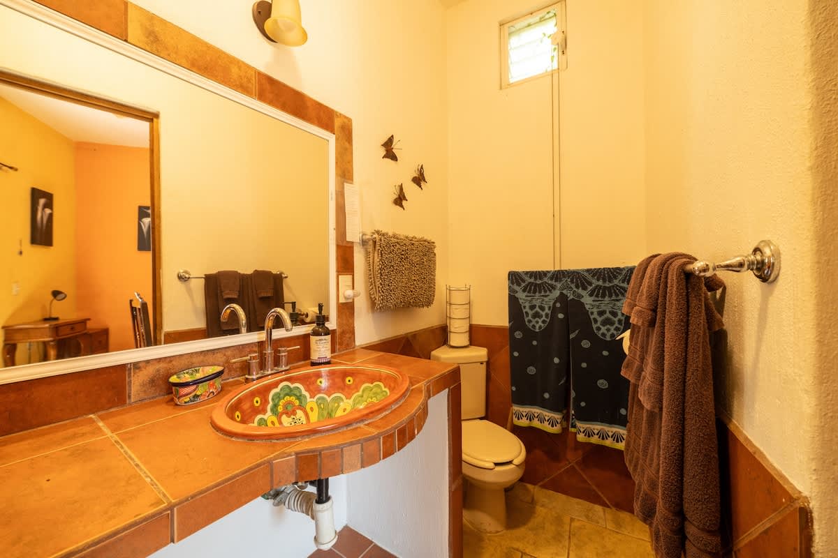 A vibrant bathroom with terracotta-tiled accents and a hand-painted basin sink on a tiled vanity. A toilet is visible next to the vanity, with towels hanging on the wall and a mirror above the sink.