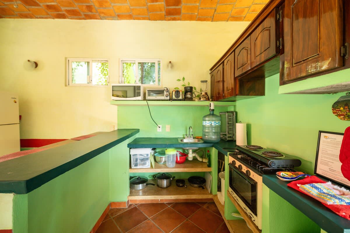 A closer view of the kitchen counter shows a gas stove with an oven, a sink, a microwave, and various cookware, all set against light green walls with a red stripe and a vaulted brick ceiling.