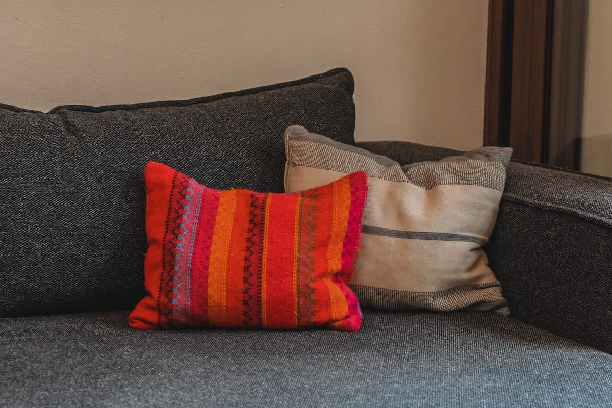 Two decorative pillows rest on a dark grey sofa; one is a vibrant red and orange striped pillow with intricate patterns, and the other is a neutral-toned striped pillow.