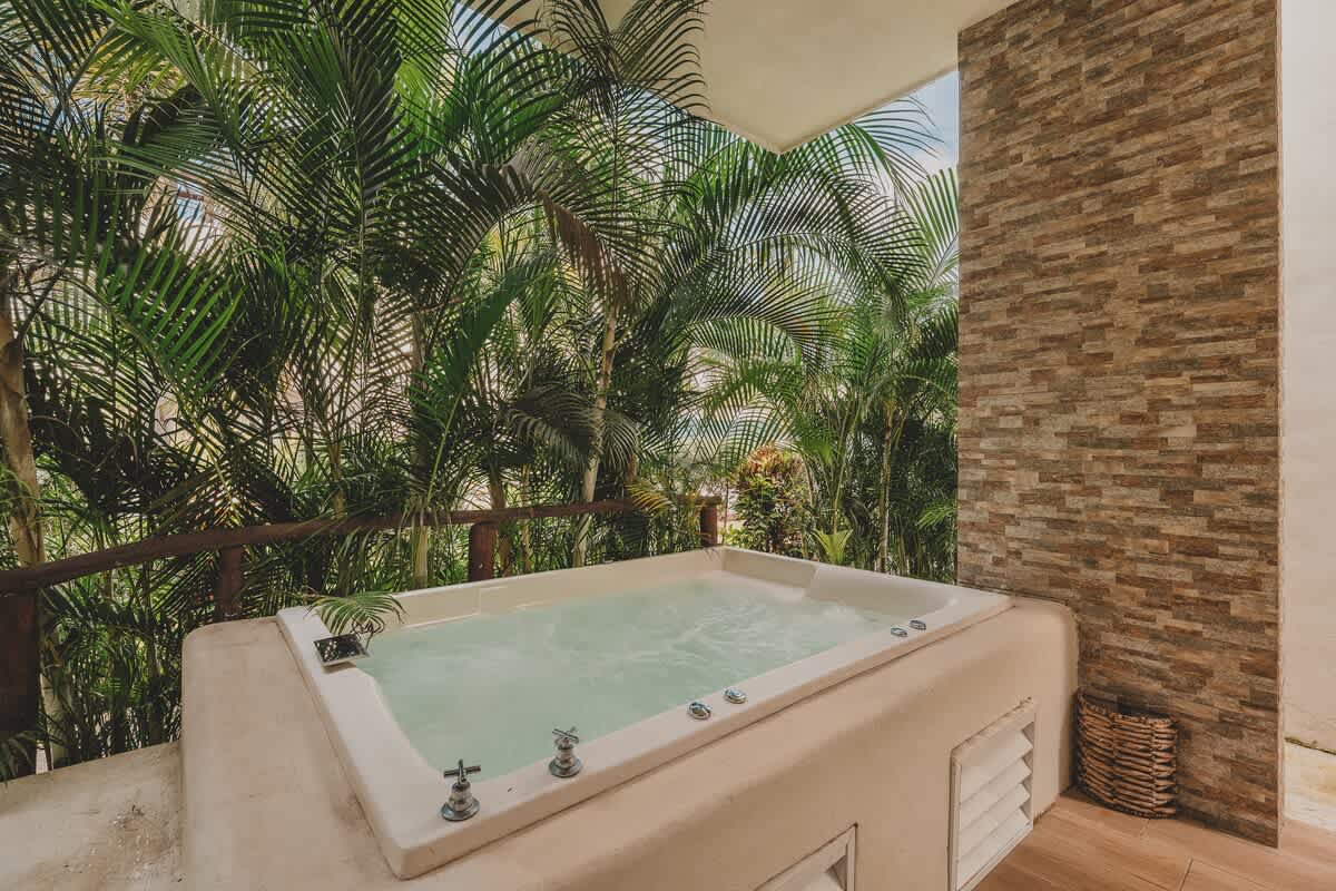 A wider view of the outdoor hot tub, showing its placement on a covered patio or balcony, with dense tropical foliage providing privacy and a natural backdrop.