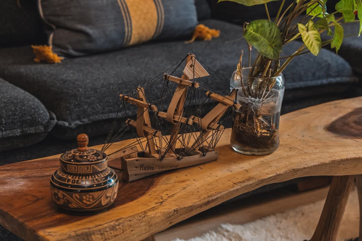 A rustic live-edge wooden coffee table displays a detailed wooden model sailboat and a glass vase holding a green plant, creating a cozy and decorative focal point.