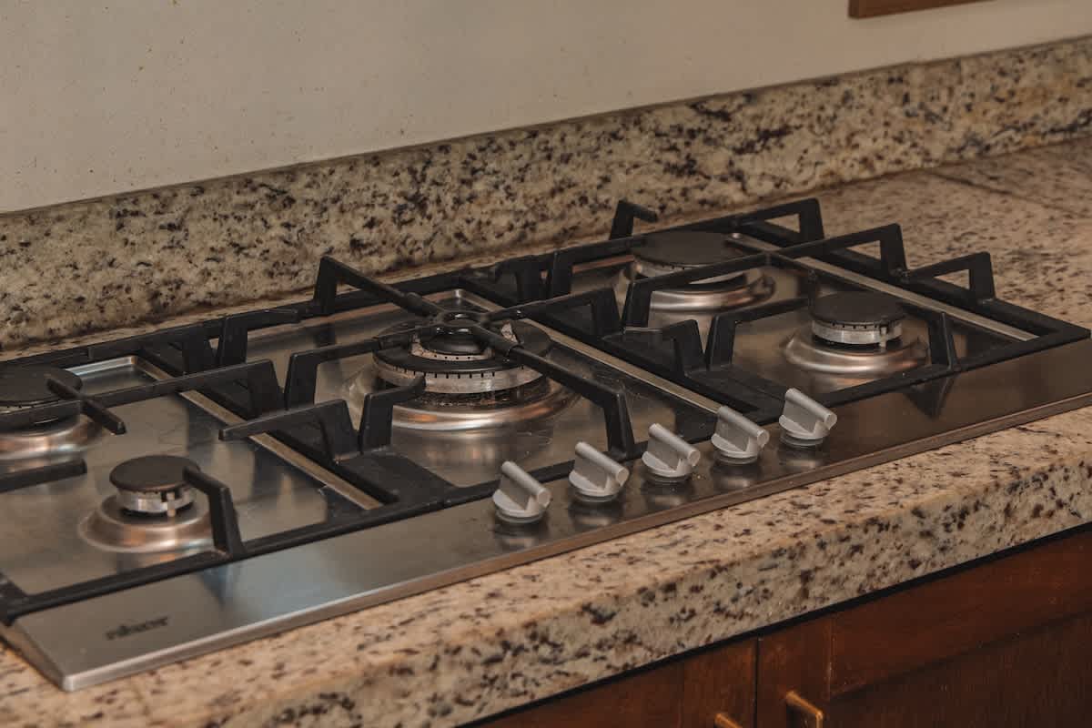 A sleek stainless steel gas stovetop with five burners and silver control knobs is integrated into a speckled granite countertop, providing a functional cooking area.