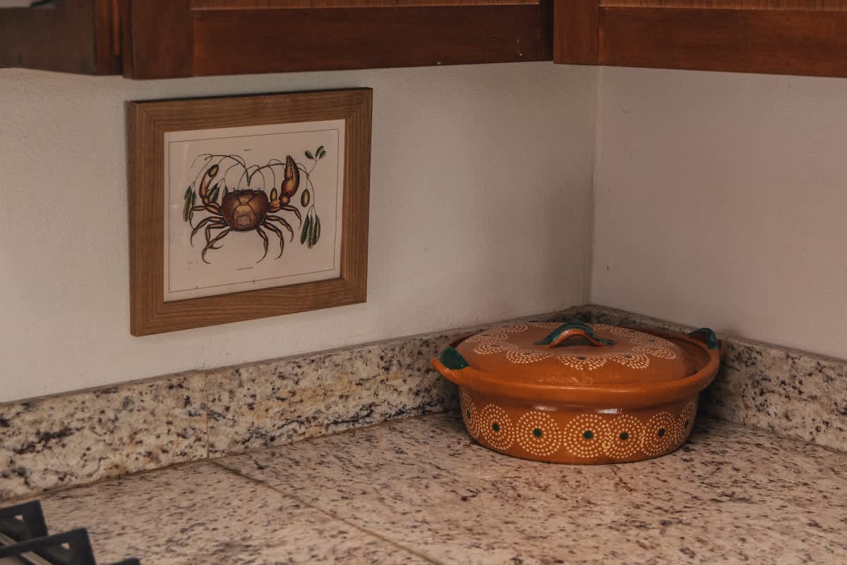A corner of a kitchen countertop features a framed print of a crab and a decorative terracotta pot with a lid, adorned with a white and green circular pattern.