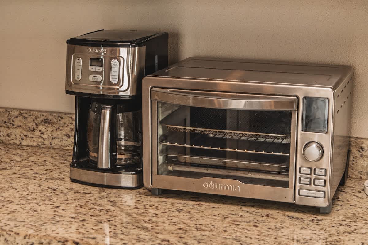 A stainless steel Cuisinart coffee maker and a matching Gourmia toaster oven sit side-by-side on a speckled granite countertop, showcasing modern kitchen appliances.