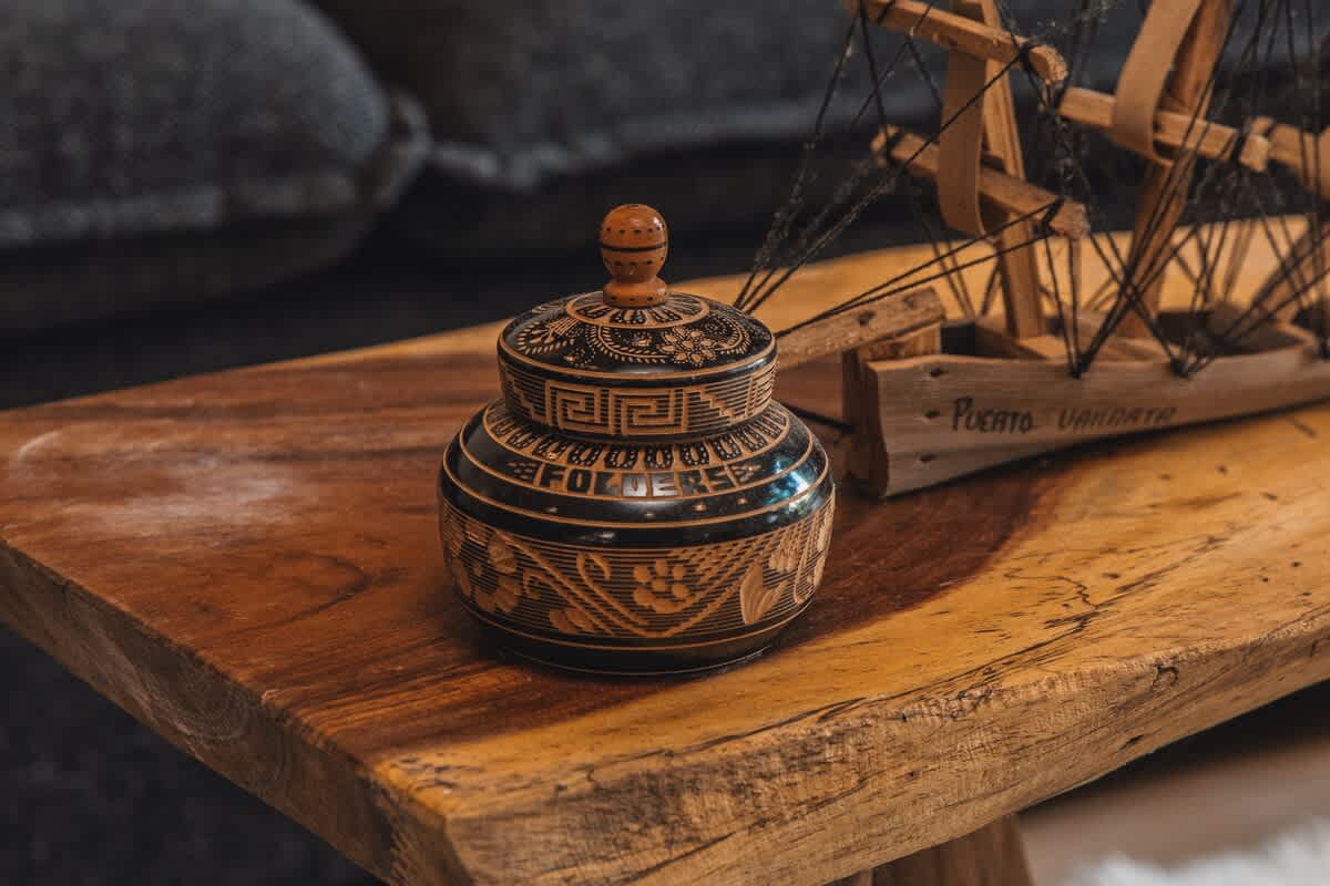 A close-up view of a decorative black and gold wooden jar with intricate carvings and a lid, sitting on a rustic live-edge wooden coffee table, showcasing detailed craftsmanship.