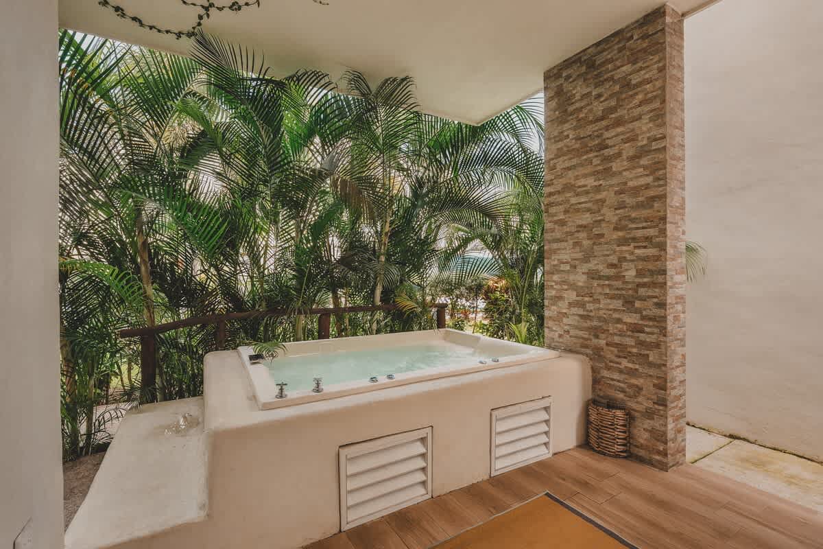 An inviting outdoor hot tub, built into a light-colored concrete structure, surrounded by lush tropical palm trees and set on a tiled balcony or patio area.