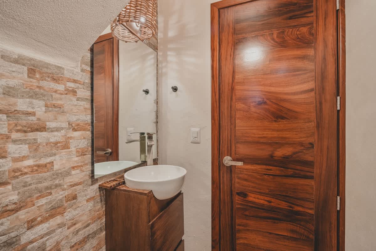 A close-up of the modern vessel sink set on a dark wood vanity, with a large mirror reflecting the room, and a woven light fixture providing warm illumination in this compact bathroom.