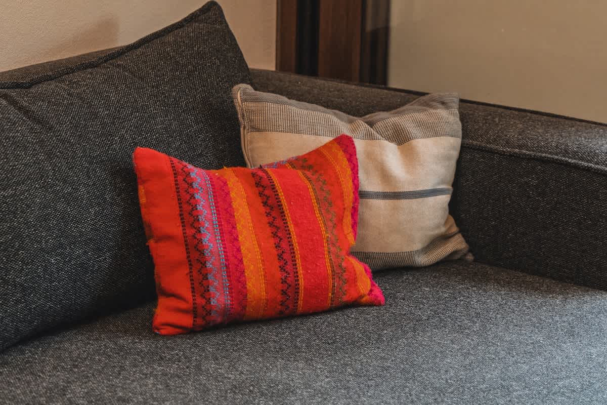 Two plush throw pillows, one in vibrant red and orange stripes and another in muted beige and grey stripes, rest on a dark charcoal grey sofa, adding comfort and color.