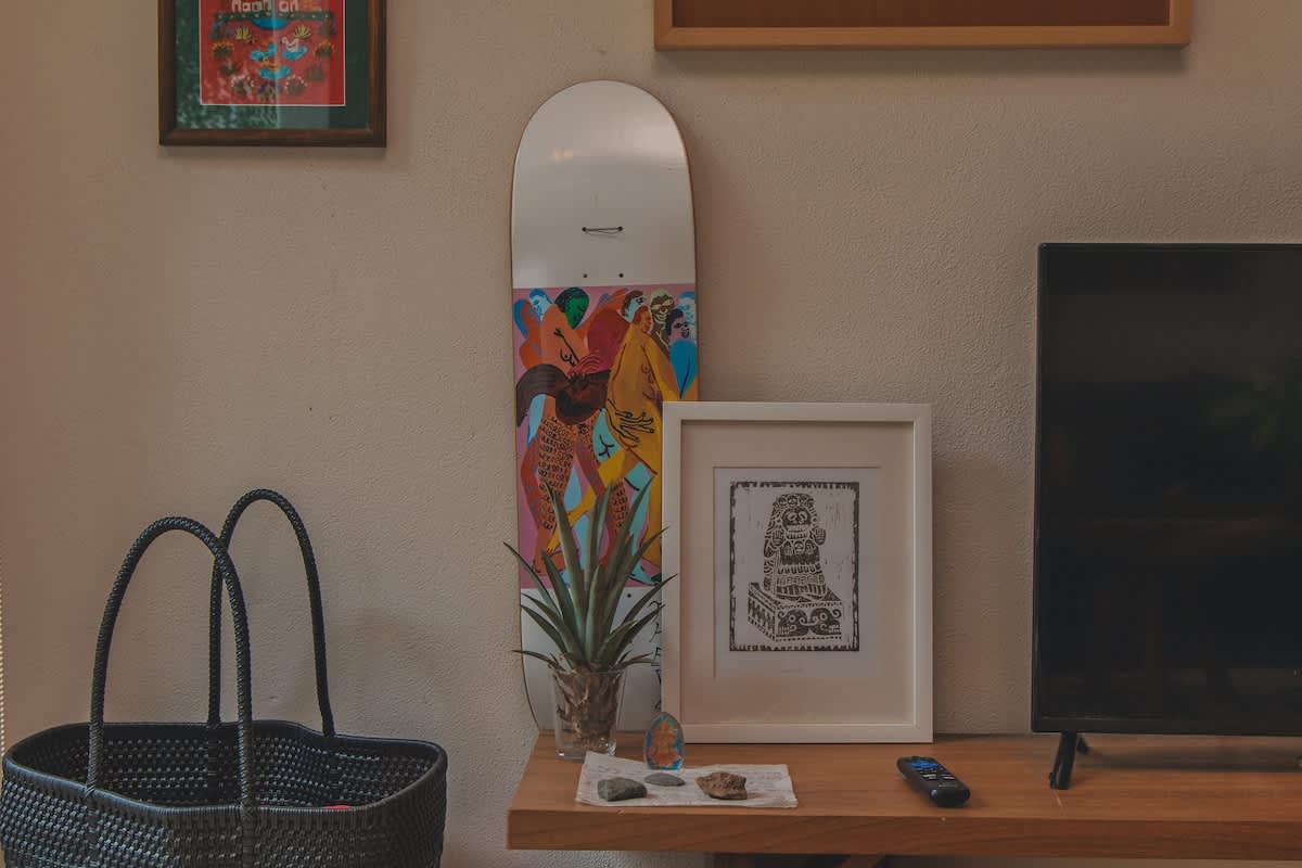 A wooden shelf holds various decorative items including a skateboard with colorful artwork, a framed black and white print, and a small potted plant, positioned next to a flat-screen television.