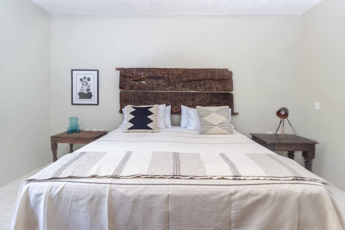 Spacious bedroom featuring a large bed with a rustic, raw-edge wooden headboard, neutral-toned bedding, two wooden nightstands, and a framed black and white artwork.