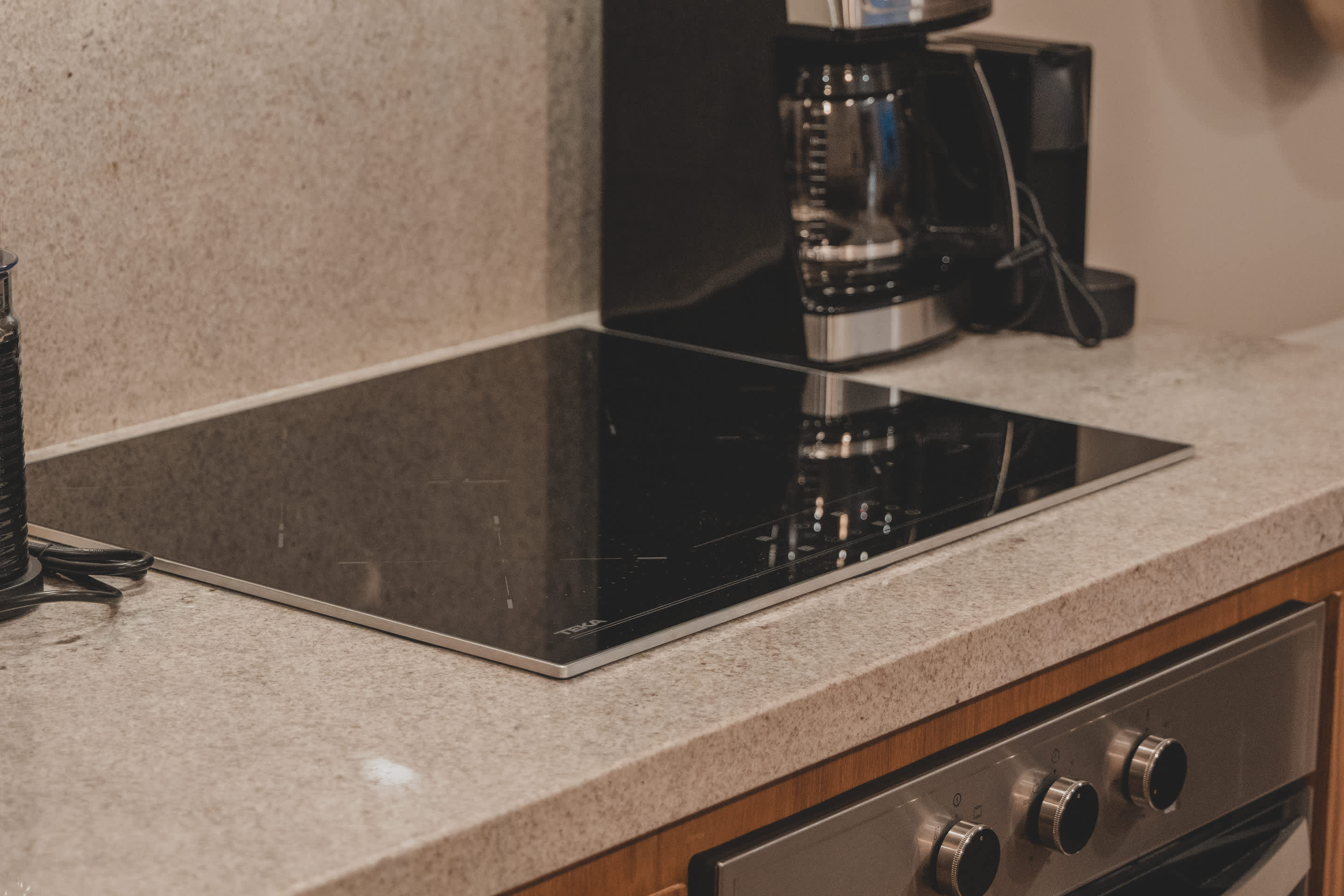 A sleek black induction cooktop is integrated into a light speckled granite countertop, with a black coffee maker and a knife block visible in the background.