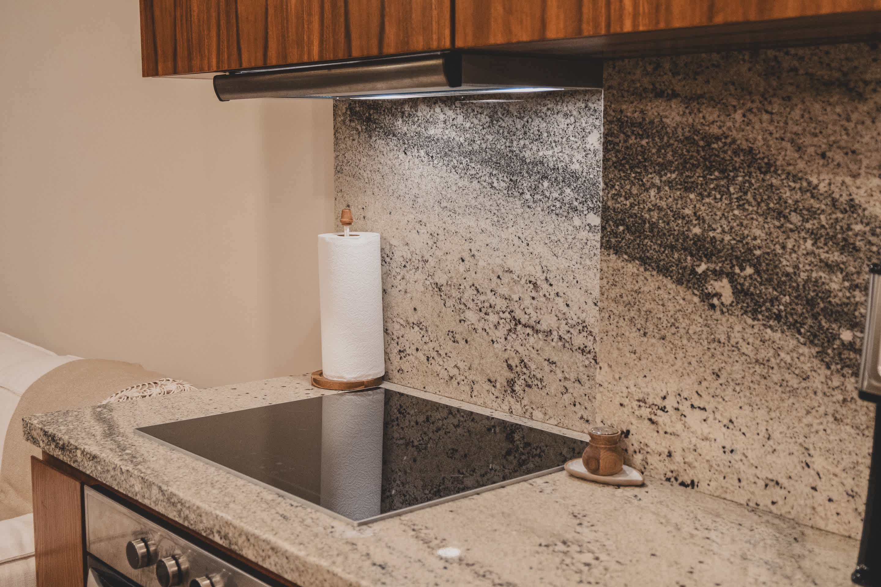 A sleek black electric stovetop integrated into a light granite countertop, with a paper towel holder nearby and a matching granite backsplash extending up the wall.
