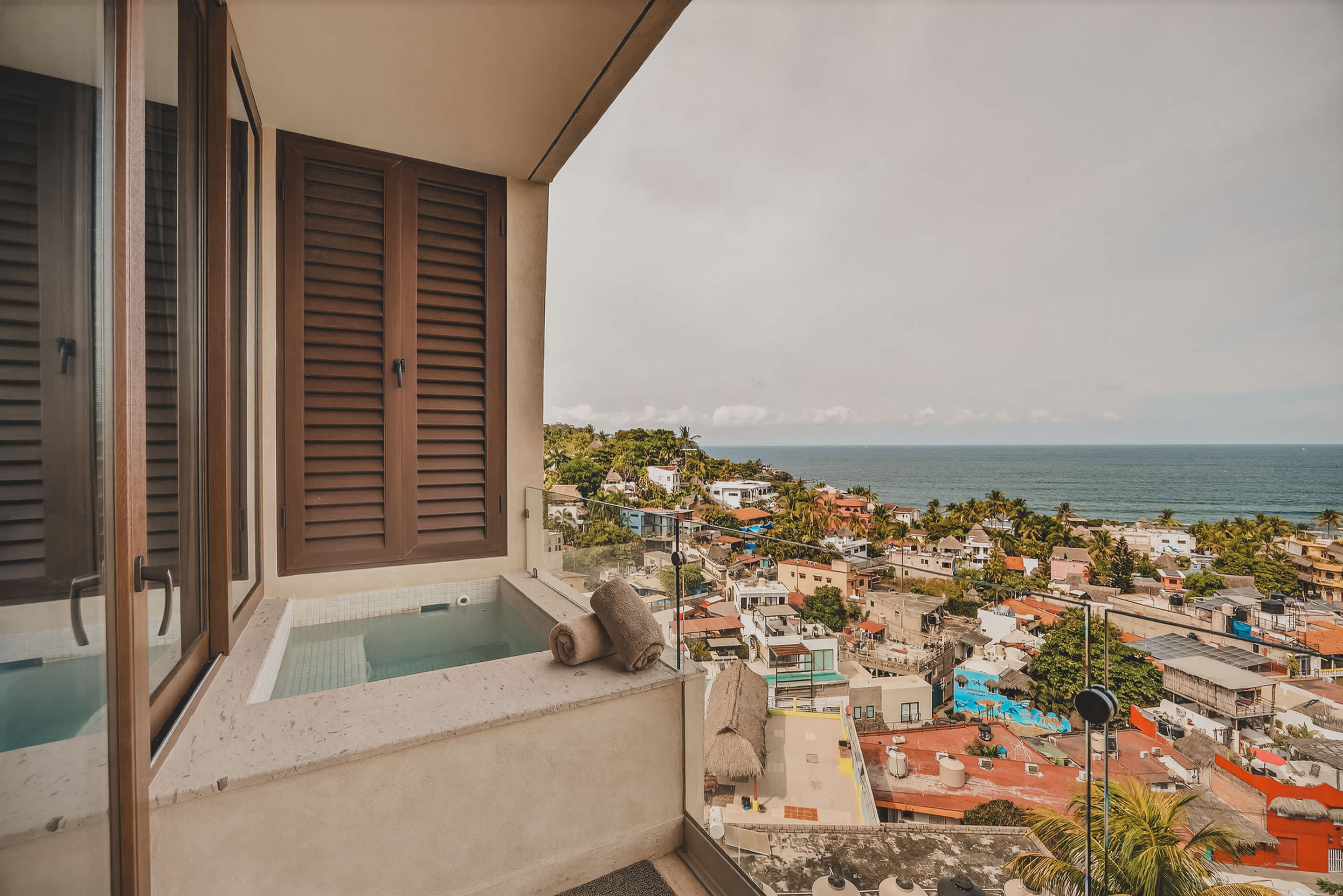 A private balcony hot tub with two neatly rolled towels provides an intimate setting with a breathtaking backdrop of a colorful coastal town and the expansive ocean.