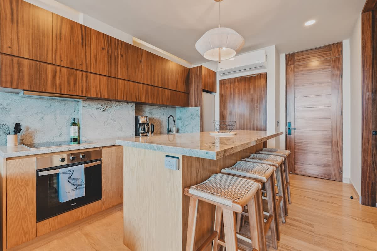 Well-equipped kitchen with light wood lower cabinets, dark wood upper cabinets, and granite countertops. It features a built-in oven, electric cooktop, and a large island with bar stools.