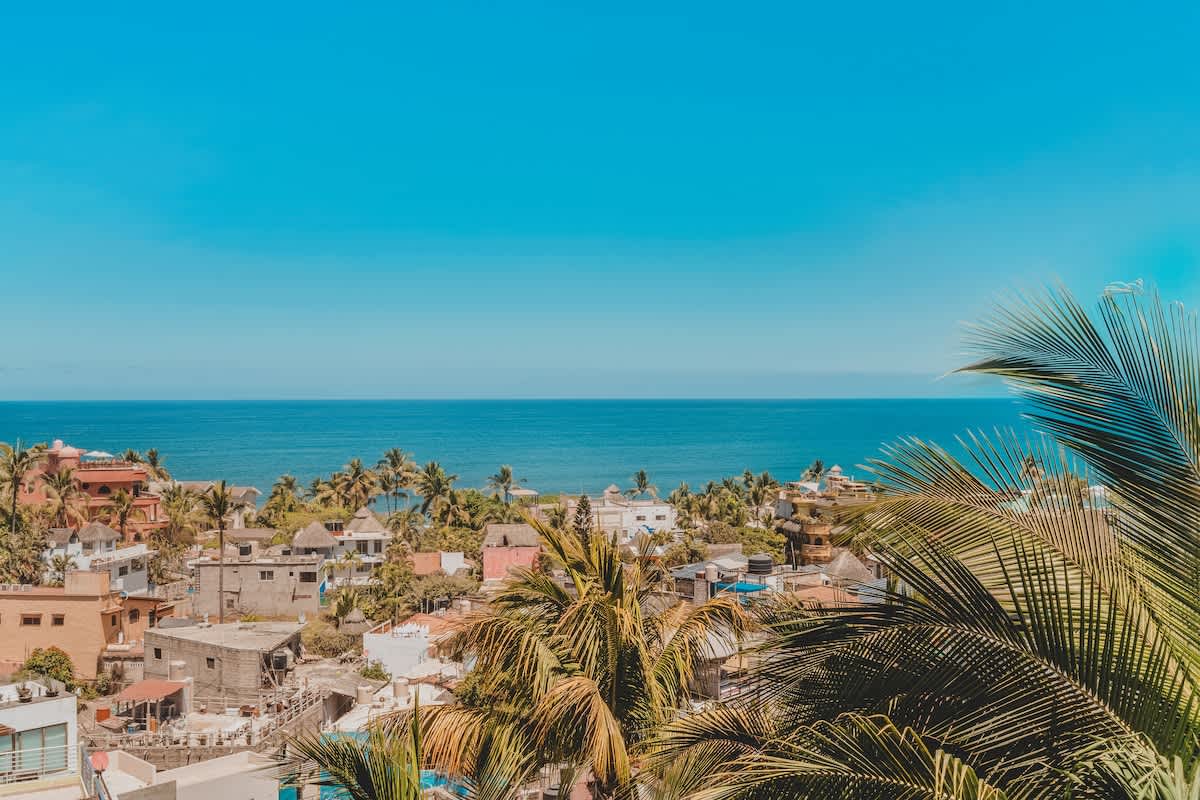 A breathtaking panoramic view from the property captures the vast blue ocean meeting the horizon, with a vibrant coastal town nestled among abundant palm trees in the foreground.
