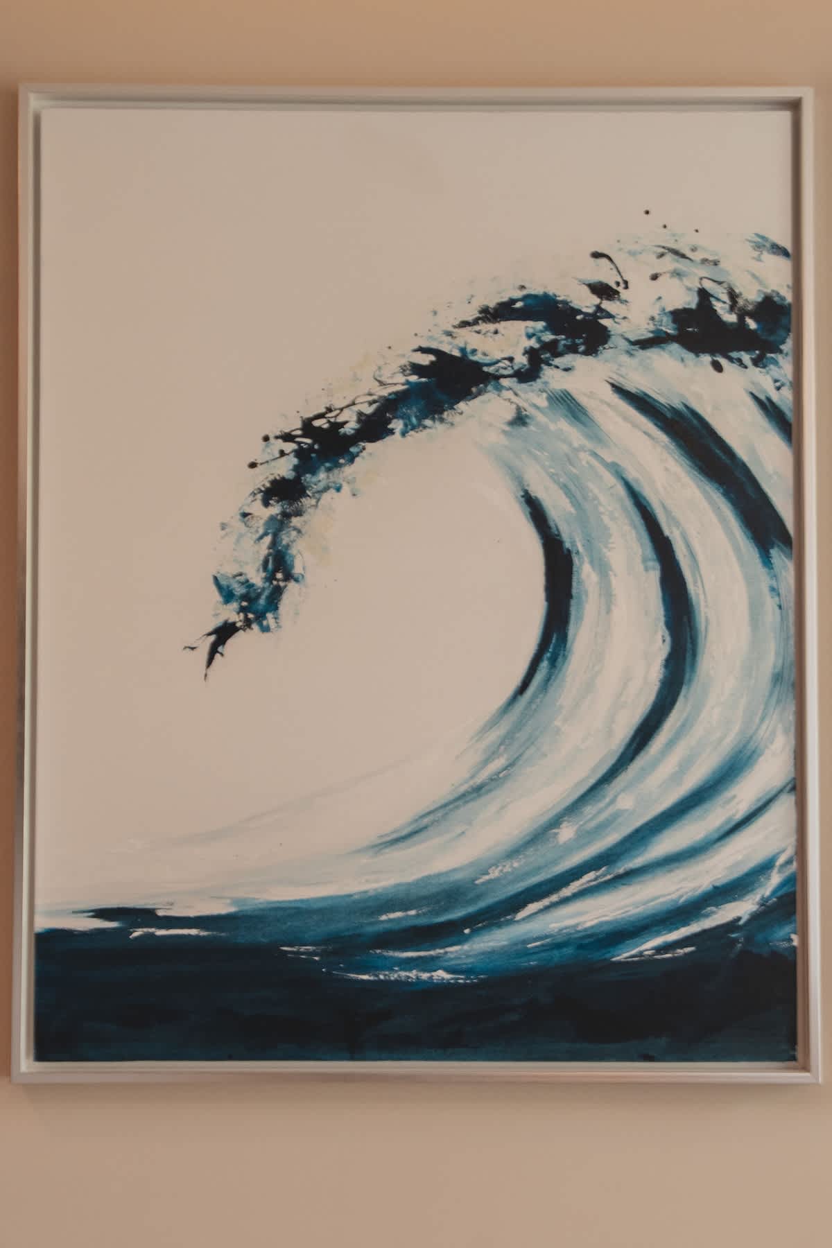 Close-up of a framed artwork featuring a powerful blue and white ocean wave, with splashes of dark blue paint, set against a light background.