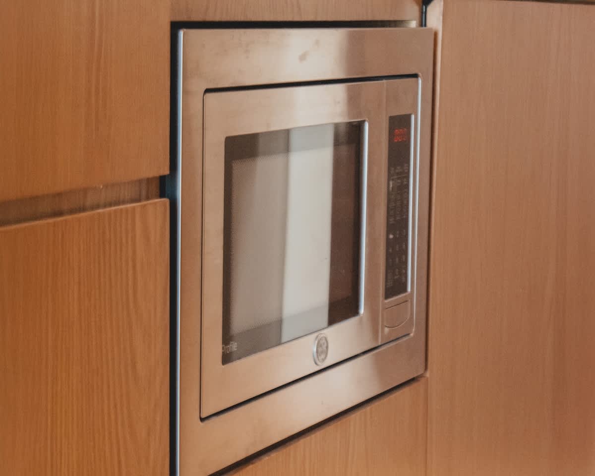 A sleek, stainless steel GE Profile microwave is built seamlessly into light-colored wooden cabinetry, showcasing a modern and integrated kitchen appliance design.