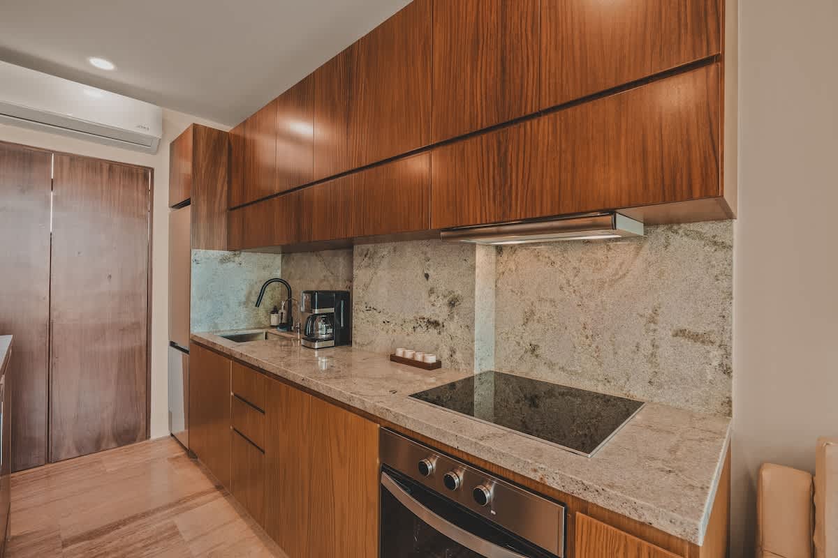 Contemporary kitchen with dark wood upper and light wood lower cabinets, granite backsplash and countertops, featuring a built-in electric stove, oven, sink, and coffee maker.