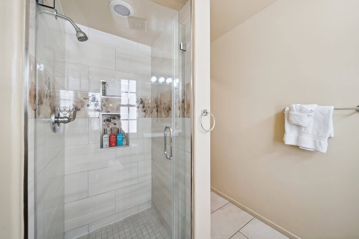 A modern walk-in shower with clear glass enclosure, light-colored tiled walls, a built-in niche for toiletries, and a rain showerhead.