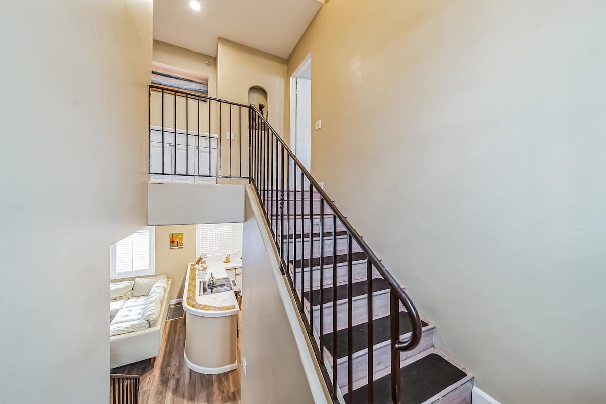 A view from the top of a staircase with dark wood treads and a black metal railing, looking down into the open-concept kitchen and living area below.